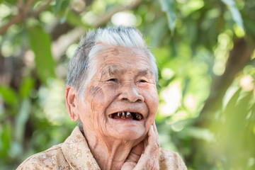 Older people for insurance concept : Portrait of Asian elder woman is smiling with her black tooth with happy at outdoor in sunny day