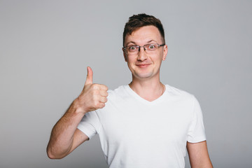 Fototapeta premium Happy successful confident man in black t-shirt showing thumbs up . Handsome young man gesturing and keeping mouth open while standing against grey background