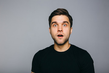 Surprised. Handsome young man standing against grey background.