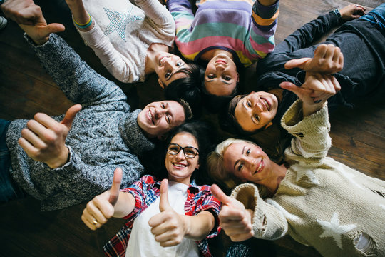 Happy friends lying together in circle looking at camera, keeping hands  and smiling while lying on wooden floor.. Concepts about friendship,lifestyle,unity,business and teamwork.