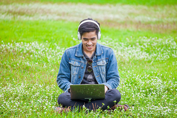 Naklejka na ściany i meble young model handsome man sitting outside in park listening music enjoying headphone with notebook , relaxing time concept