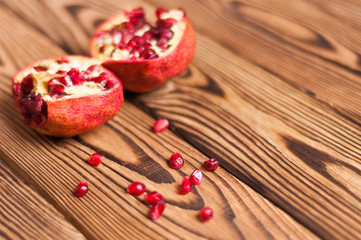 Fototapeta na wymiar Scattered fresh ripe red seeds of pomegranate near two half pomegranate on old brown weathered wooden planks