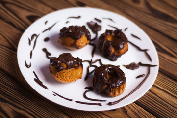 Four baked cupcakes with chocolate cream on white ceramic dish on old rustic brown weathered table