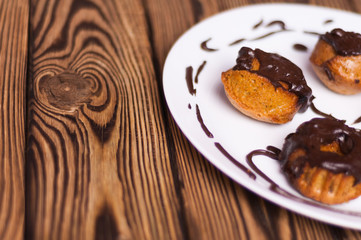 Baked cupcakes with chocolate cream on white ceramic dish on old rustic brown weathered table