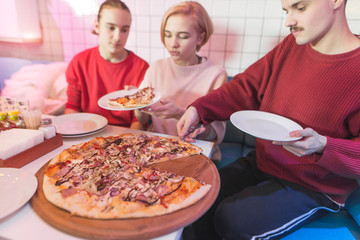 A group of friends sits in a pizzeria and eats a big pizza. Young people eat pizza at the restaurant on weekends.