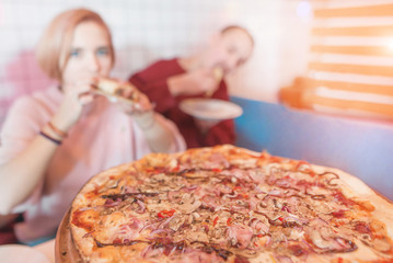 Delicious pizza on the background of a young couple. A couple eating a pizza in a cafe. Pizza is in focus, people are blurred. Place for text.