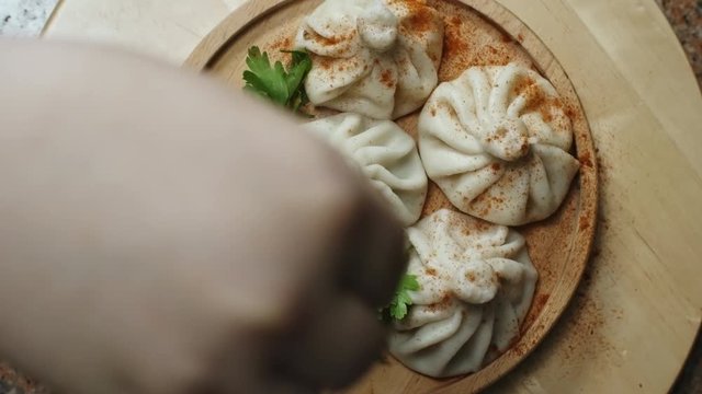 Top view of unrecognizable cook seasoning delicious khinkali dumplings lying on spinning wooden plate