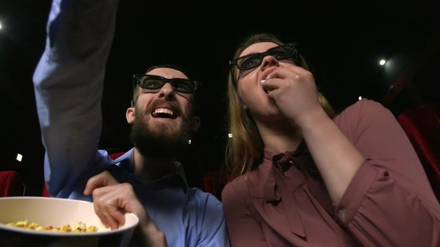 Close up of attractive young couple laughing at the movie theater. Caucasian girl and her boyfriend watching funny comedy at the cinema. Pretty female viewer tilting her head forward