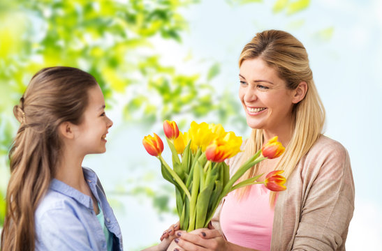 people, family and holidays concept - happy daughter giving tulip flowers to her mother over green natural background