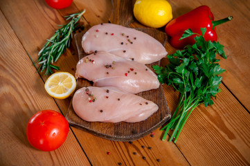 raw chicken fillet on a wooden cutting board with vegetables and spices