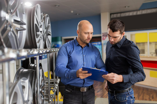 business, maintenance and people concept - male customer choosing alloy wheel rims and salesman with clipboard at car repair service or auto store