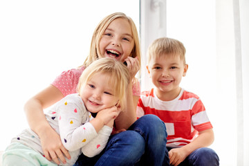 childhood, leisure and family concept - happy little kids hugging at window