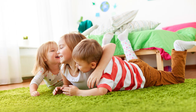 childhood, leisure and family concept - happy little kids lying on floor or carpet