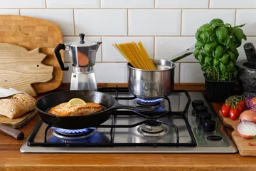 Poster Pan fried salmon fillet and spaghetti on a gas stove in traditional home kitchen. Wood worktop. © Moving Moment