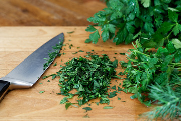 Freshly chopped up bunch of parsley on wood chopping board next to kitchen knife.