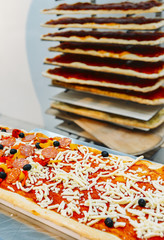 Uncooked rectangular Roman style pizza with salami topping