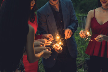 friends enjoying sparklers in the night party. Group of friends playing fireworks together. Selective focus on hand of man holding lighter.