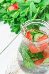 Glass Jug with Fresh Cool Infused Detox Water with Ripe Organic Strawberries Sliced Cucumbers Mint. White Plank Wood Background. Healthy Drink Detox Summer Refreshment. Copy Space