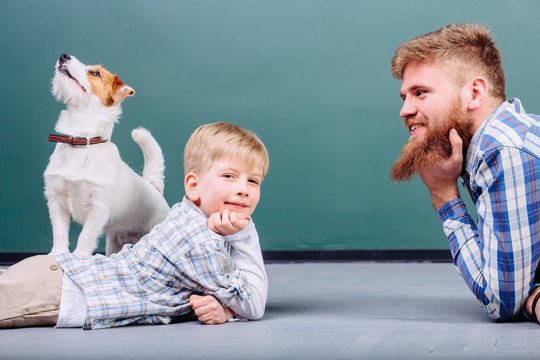 Happy Caucasian family having fun in their new home playing with puppy dog jack russell terrier. Hansome beard father and his preschooler son lying on the floor in front of each other. Side view