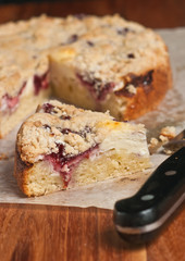 Top view, close up of a slice of freshly baked, homemade, raspberry cream coffee cake on a sheet of parchment paper with  the handle of a chef's knife on a wood, cutting board 