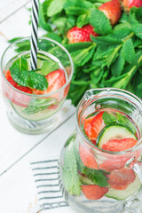 Fresh Cool Infused Detox Water with Ripe Organic Strawberries Sliced Cucumbers Mint in Glass and Jug. White Plank Wood Background. Healthy Drink Detox Summer Refreshment. Copy Space