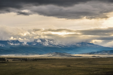 Cloudy snowed mountain peaks in sunset. Altai, Siberia, Russia