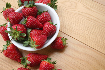 Fresh strawberries in a bowl on wooden background