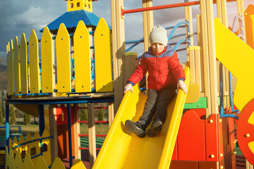 Happy little boy have fun and sliding on colorful modern playground in park.