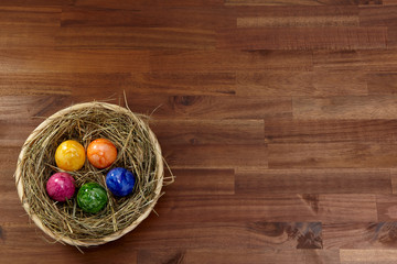 Korb mit Heu und bunten Eiern auf Holz aus Akazie