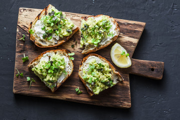Avocado and ricotta toast with micro greens on a cutting board, on a dark background, top view. Good fats healthy eating concept. Delicious breakfast or snack