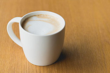 Coffee latte with milk foam in white mug on the wooden table.