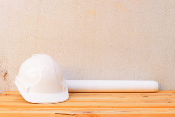 white safety helmet plastic and paper roll plan blueprint construction of engineering on wood floor table background with copy space add text