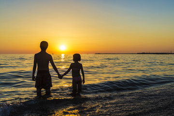 Little girl and teenager bathing on a beach at sunset