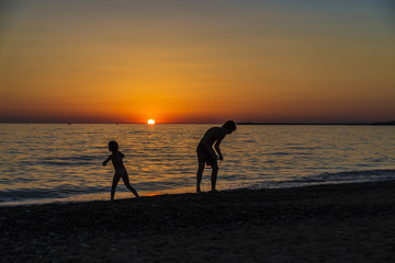Fototapeta premium Little girl and teenager playing on a beach at sunset