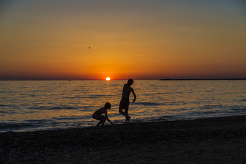 Little girl and teenager playing on a beach at sunset