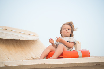 Kid with blond hair have fun outdoor. Child sit in ring buoy on sunny day. Little boy with lifebuoy on tropical beach. Summer vacation and leisure. Safety, rescue and help concept