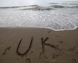 UK text written on the sand of the beach near the sea