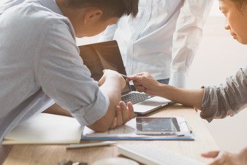 Business start up team working together. Young business people in casual talking about business plan and pointing at computer screen to explain to colleagues.