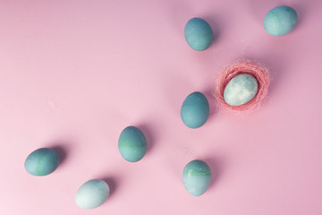 Several different shades blue eggs and blue egg decorated with pink sisal nest on the minimalist pink background