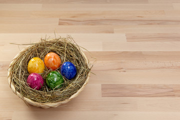 Korb mit Heu und bunten Eiern auf Holz aus Buche