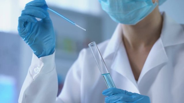 Female lab worker dripping blue liquid in test tube and analyzing reaction