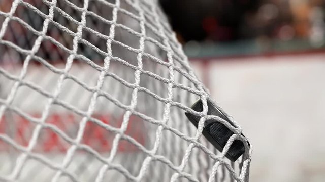Hockey puck flies into the net on a hockey boards with a red stripe. The movement at the beginning is accelerated then slowly