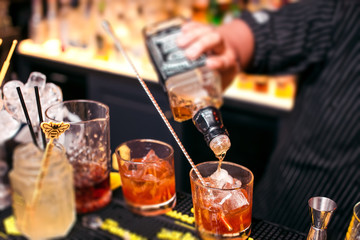 Bartender adding whiskey from bottle into the cocktail glass with ice cubes on the bar counter with bar equipment. Barman working.