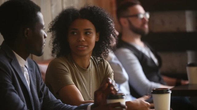 Diverse millennials working relaxing in cozy cafe, smiling african couple having pleasant conversation, multi-ethnic young people enjoying friendly atmosphere sitting at coffee shop table, lunch time