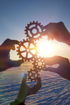 Four hands of businessmen collect the gear from the gears of the details of the puzzles. against the background of sunlight. Concept business idea. Teamwork, cooperation, strategy