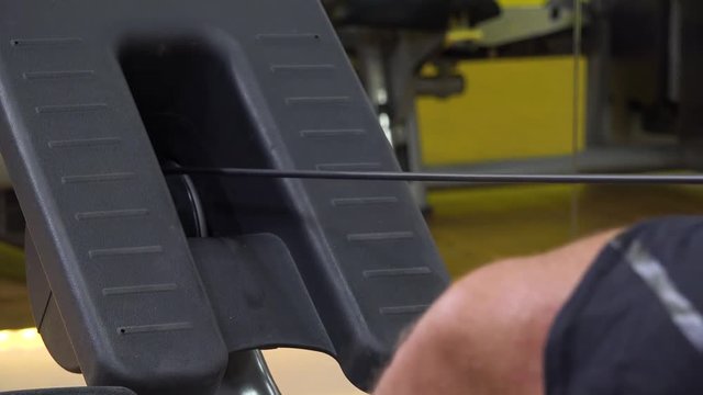 A fit man trains on a rowing machine in a gym - closeup