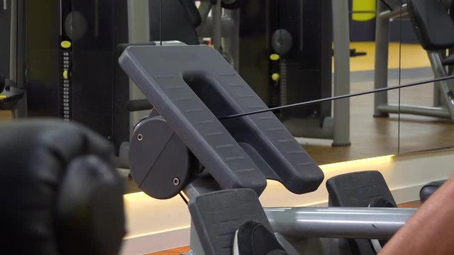 A fit man trains on a rowing machine in a gym - closeup