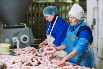 Butchers processing sausages at meat factory.