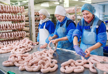 Butchers processing sausages at meat factory.