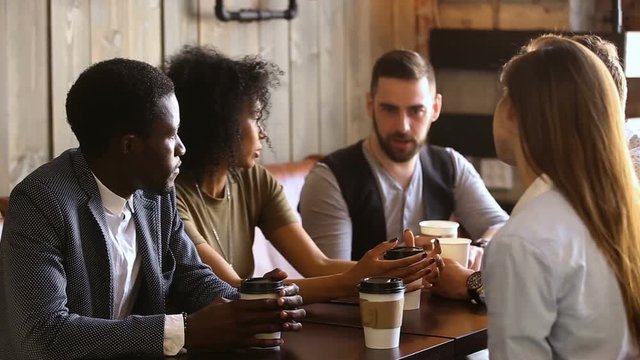Multiracial friends drinking coffee together in cozy cafe, mixed race buddies talking sharing news having fun at meeting in cafeteria, diverse millennials chatting spending time in bar after work